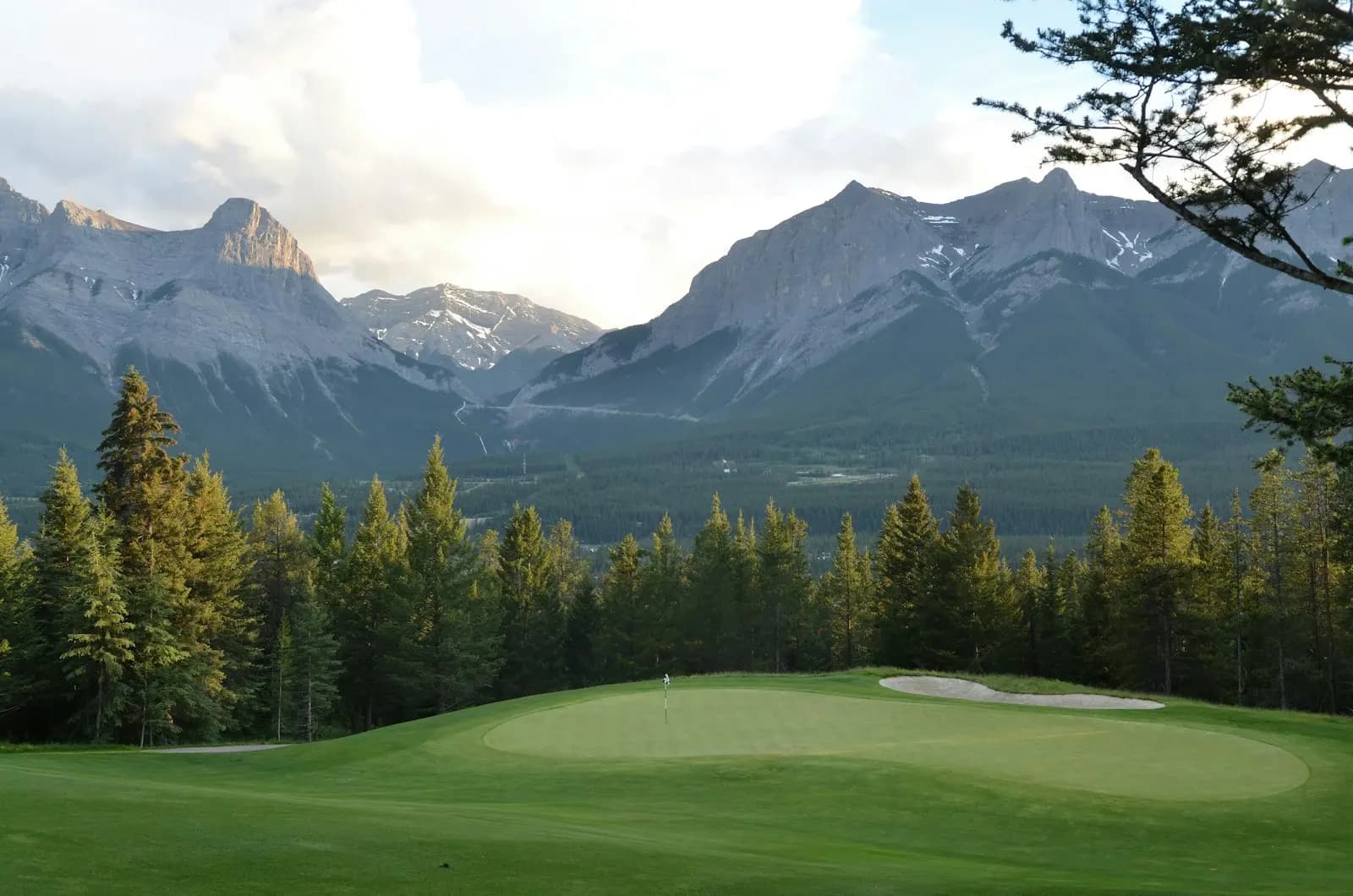 A mountain golf green framed by pines and dramatic peaks